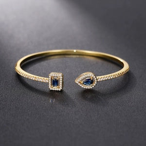 Detailed close-up of golden adjustable cuff with pear-cut blue gem and white zirconias