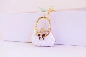 Detailed close-up of a gold metal keychain shaped like a white handbag with rhinestones