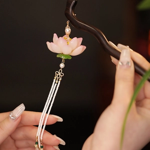 Dettaglio di un fermaglio per capelli in legno con loto rosa e nappe di perle