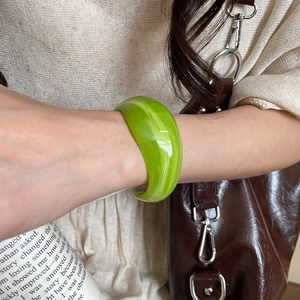 Macro shot of wide translucent green acrylic bangle with marble textures on wrist