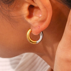 Two-tone gold and silver stainless steel hoop earrings worn by a model in a close-up shot