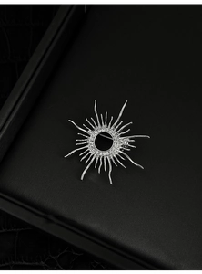 Detailed macro view of silver sunburst brooch with liquid metal rays on black leather box