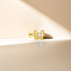 Macro shot of a golden bow-shaped S925 silver ear stud with a clear round gemstone detail