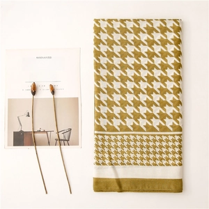 Flat lay of mustard yellow houndstooth scarf with fine striped edges on a white backdrop