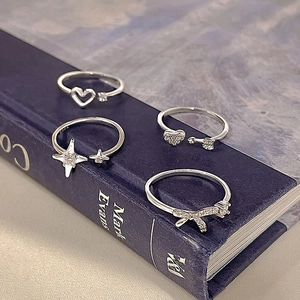 Set of four S925 silver rings with zircon heart, star, and bow designs on blue book