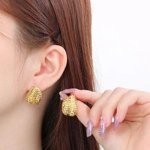 Close-up of golden irregular drop earrings with beaded texture and sparkling rhinestones