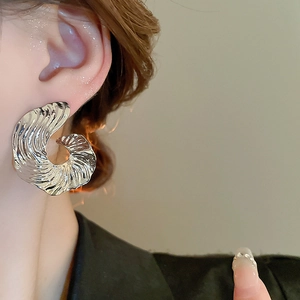 Close-up of silver-tone spiral stud earring with textured wavy patterns on model