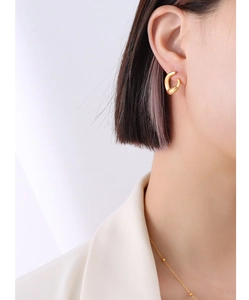 Close-up of a model wearing minimalist thick double-loop 18k gold-plated steel earrings
