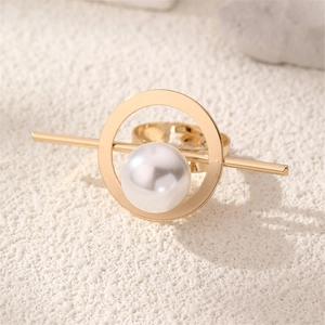 Macro detail of geometric gold ring with central white pearl on a textured background