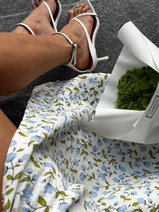 Close-up of white strappy high heel sandals with ankle buckle and elegant floral cotton dress