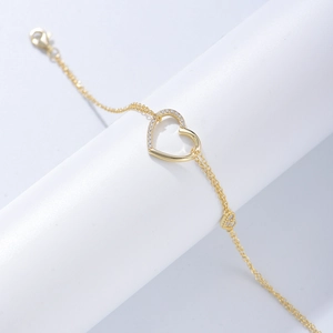 Détail du bracelet doré à double chaîne avec un charm en forme de cœur serti