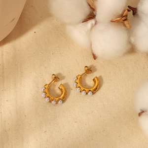 Élégantes créoles en forme de C plaquées or 18 carats avec perles sur fond de lin beige