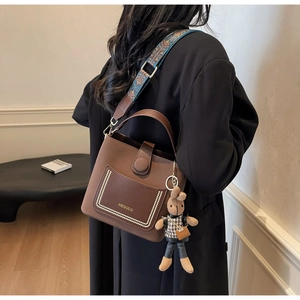 Brown bucket bag with wide ethnic pattern strap and knitted rabbit charm shown on model