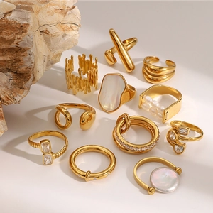 Set of 11 gold stainless steel rings with shell, pearls, and zircons on white stone