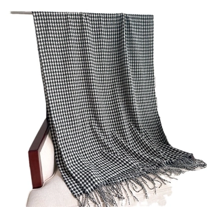 Classic black and white houndstooth cashmere scarf with tassel fringe on a wooden chair