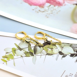 Detail of golden chain earrings with black moon pendants on a floral paper background