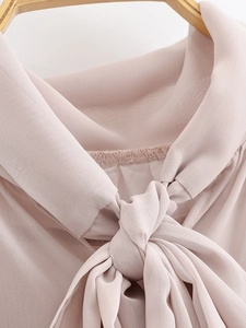 Detail view of the tie-neck bow and light chiffon fabric of the lotus pink dress