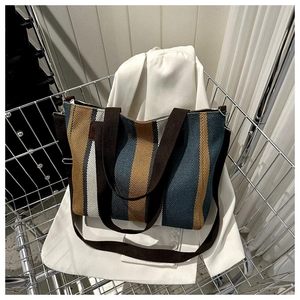 Detailed view of large striped knit tote bag with brown canvas handles in a metal cart
