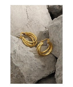 Macro detail of triple-layered gold-plated S925 silver hoop earrings on a gray rock base