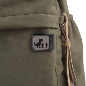 Dettaglio macro di borsa in tela verde militare con spilla dinosauro pixel TV retrò