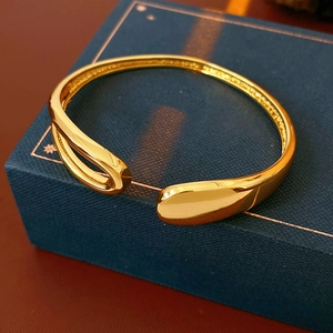 Macro view of gold-plated water drop open bangle on a deep blue jewelry box