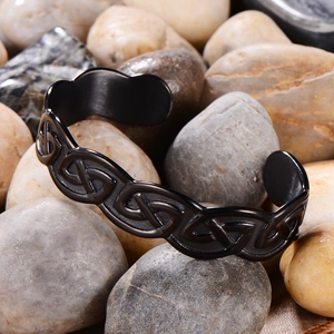 Close-up of matte black Viking Celtic knot open cuff bracelet on river pebbles