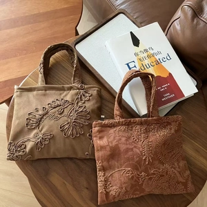 Detail of vintage embroidered suede tote bags with floral patterns on a wooden table