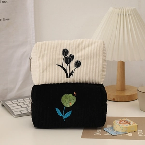Close-up of corduroy makeup bags with floral embroidery in off-white and black