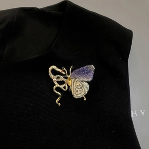 Macro detail of a crystal-encrusted snake and purple embroidered butterfly brooch