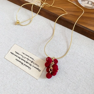 Detailed view of gold chain necklace with deep red flocked grape pendants on linen