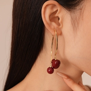 Detail of red cherry resin drop earrings on a model with golden metallic curves