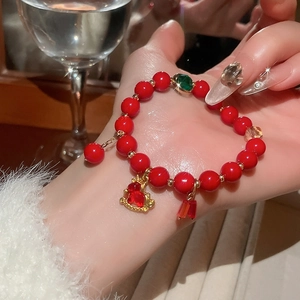 Close-up of red beaded bracelet with gold heart pendant and green gemstone charms