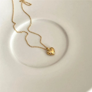 Detail showing a gold heart necklace with tiny zircons on a white ceramic plate