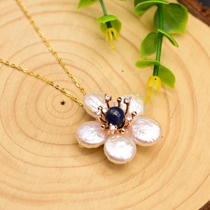 Baroque pearl flower necklace with blue gemstone center on gold chain over rustic wood