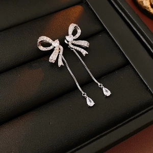 Detail of silver bow tassel earrings with heart and teardrop zircons on black tray