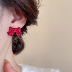 Close-up of a woman wearing vintage red bow stud earrings with a velvet-like matte finish