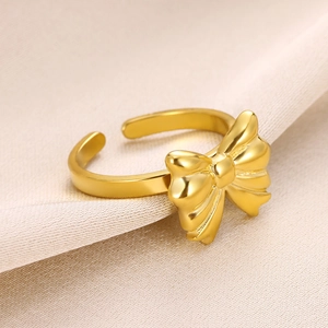 Macro shot of gold bow ring with textured finish on elegant beige silk fabric background