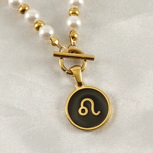 Macro detail of 18K gold necklace with Leo zodiac pendant and faux pearl bead chain