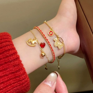 Close-up of red rope bracelets with gold zircon horse charms and traditional coin pendants