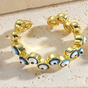 Close-up of gold adjustable ring with blue evil eye enamel charms on stone texture