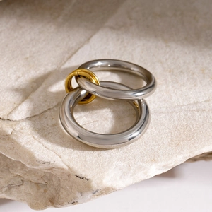 Close-up of interlocking 18k gold and silver stainless steel rings on white stone