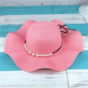 Detail of pink straw sun hat featuring elegant faux pearl chain and black ribbon bow
