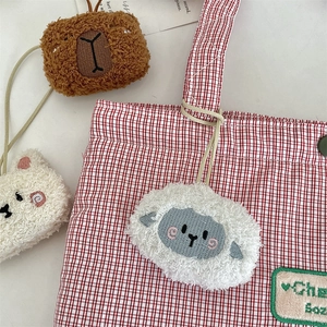 Dettaglio di ciondoli in peluche ricamati attaccati a una borsa tote a quadretti