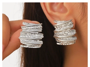 Close-up of irregular rectangular silver earrings with crinkled texture worn on ear