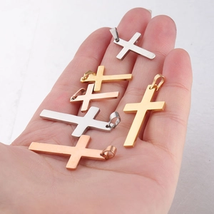 Détail de pendentifs croix en acier poli en couleurs or, argent et or rose sur la main