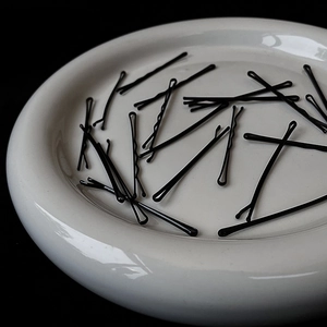 Close-up of wavy black metal hair pins on a white ceramic tray in minimalist style