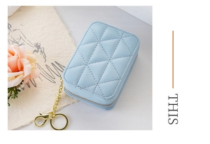 Close-up of sky blue quilted mini lipstick bag with gold chain and keychain on white fabric
