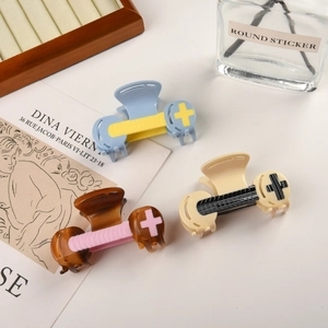 Three acetate hair claws with contrast cross design displayed on a wooden jewelry stand