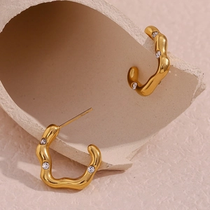 Close-up of gold plated wavy earrings with sparkling crystals on textured ceramic tray