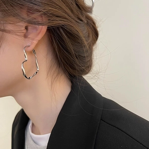Boucle d'oreille cœur torsadée argentée sur mannequin au style minimaliste et grande taille